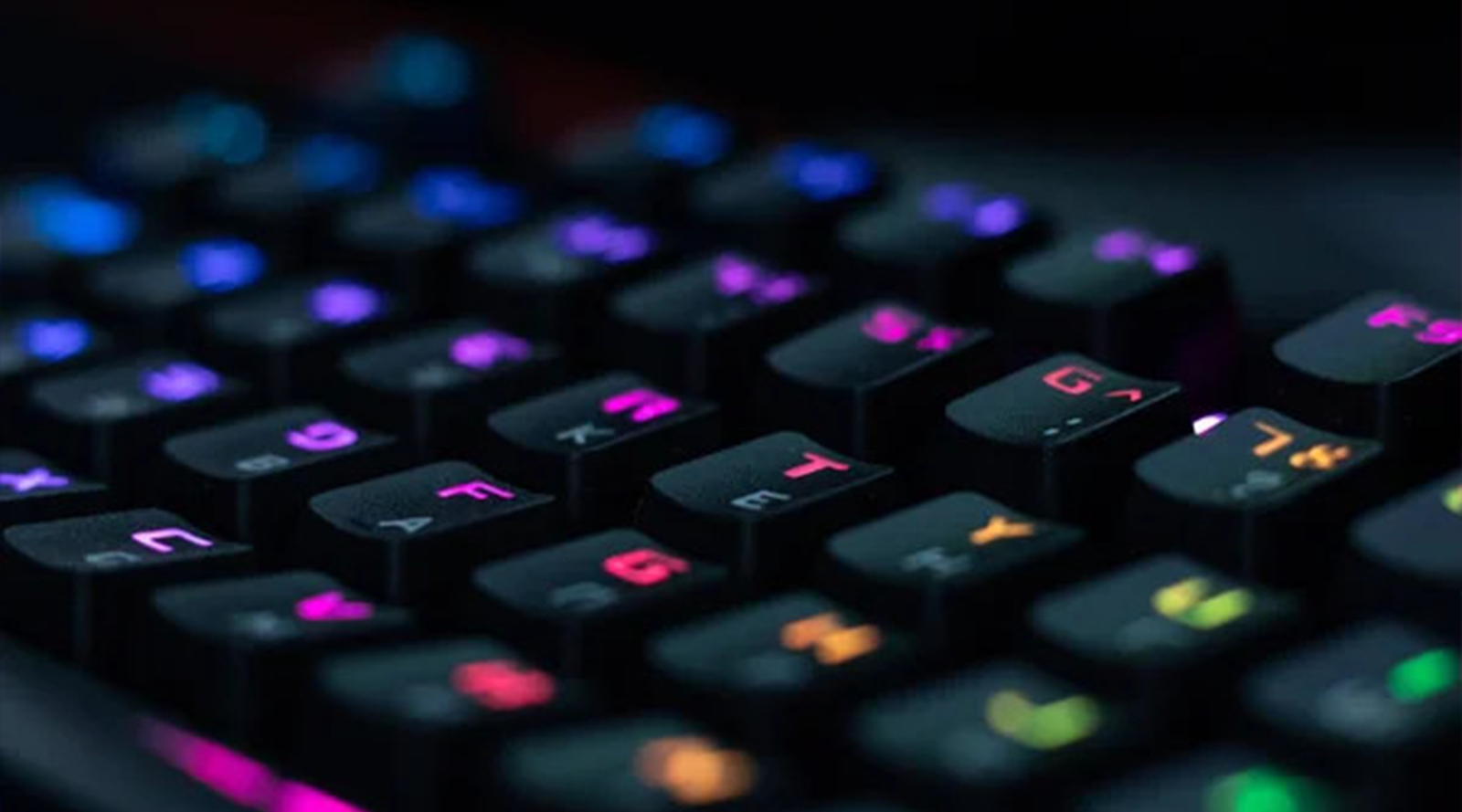 Close-up of a backlit mechanical keyboard with colorful illuminated keys in low light.